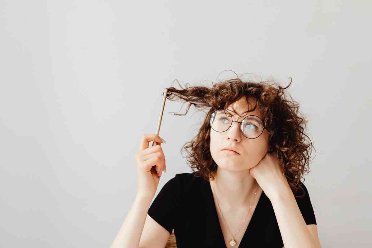 A person pausing in thought, twisting a strand of hair, gaze drifting upward in worry, the inward spiral the Eight of Swords describes
