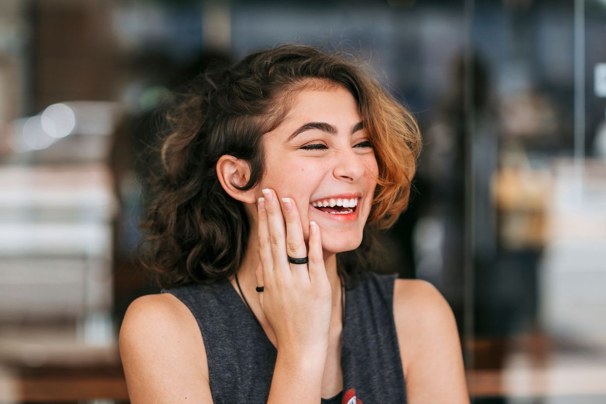 A woman smiling at her phone while sitting by a window in the morning light